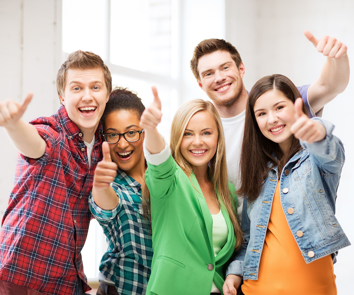 A group of young adults giving thumbs up in a classroom setting.